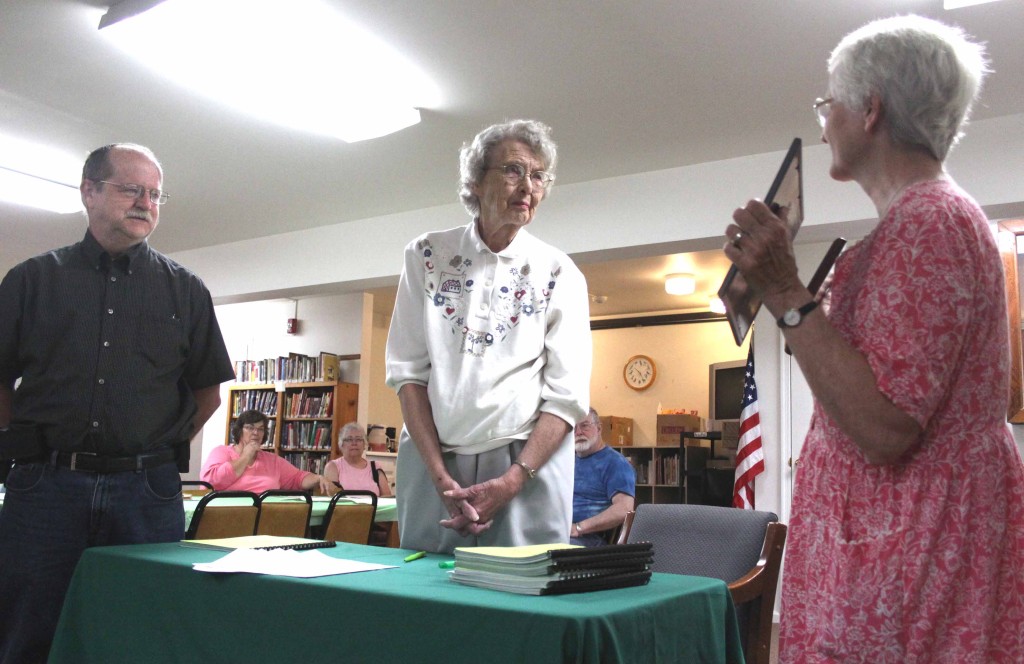 Hartwick Town Historian Carol Goodrich, right, presents Anita Harrison, one of the original prime movers of the Hartwick Historical Society, with a plaque honoring her role in ensuring the society found a home of its own in 1989.  The presentation was made today at a ceremony marking the 25th anniversary of the building, which is an addition to the Kinney Memorial Library in Hartwick hamlet.  At left is Town Supervisor David Butler.  When the society formed in 1969, "the dream was a have a permanent home."  It took 20 years, but "the dream came true," she said.  Mrs. Harrison's husband Bill, children, grandchildren and great-grandchildren were present to see her honored.  Society President Caren Kelsey made the surprise complete.  (Jim Kevlin/allotsego.com)