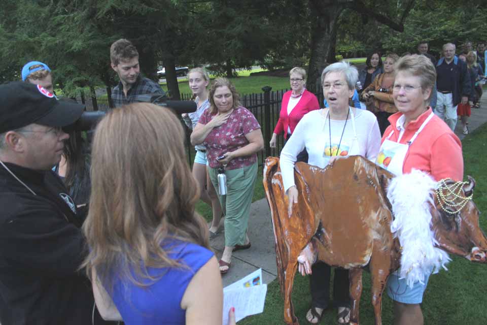 Lynn Weir, left, and Teri Sammis, brought along a bovine friend to promote the Cooperstown Farmers Market "Local Foods, Local Spirits" celebration on this morning's "Today" show.  They are interviewed by a Utica TV crew outside The Otesaga.  (Jim Kevlin/allotsego.com)