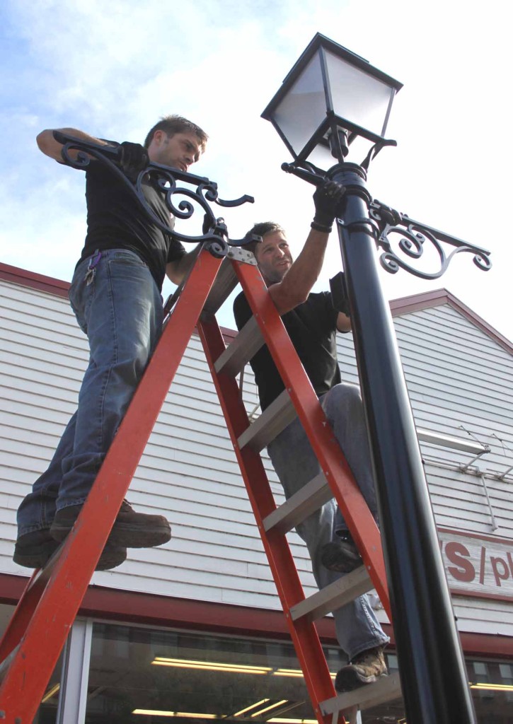 Brothers Travis and Jacob  Granger of Eastern Energy Solutions, Afton, began installing eight refurbished streetlights on Main Street, part of the $2 million downtown redo.  The fixture are the same, but have been cleaned and painted, and the 175-watt bulbs replaced with 45-watt LLED bulbs, longer lasting and more energy efficient, according to  Trustee Cindy  Falk, chair of the trustees' Streets Committee, who was at the scene with Public Works Superintendent Brian Clancy.   GFI circuits, which trip in case of problems, are safer and more energy efficient as well, Falk said.  (Jim Kevlin/allotsego.com)