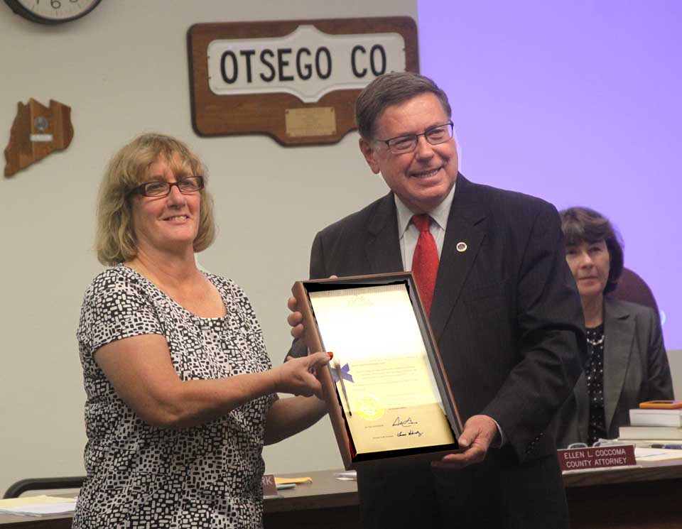 State Sen. Jim Seward, R-Milford, presents county Board Chair Kathy Clark, R-Otego, with the pen Governor Cuomo used to sign the legislation that abolished MOSA, the three-county solid waste authority that had locked in the county's garbage stream to an expensive disposal regimen. The presentation was this morning at the county board's monthly meeting in Cooperstown. (Jim Kevlin/allotsego.com)