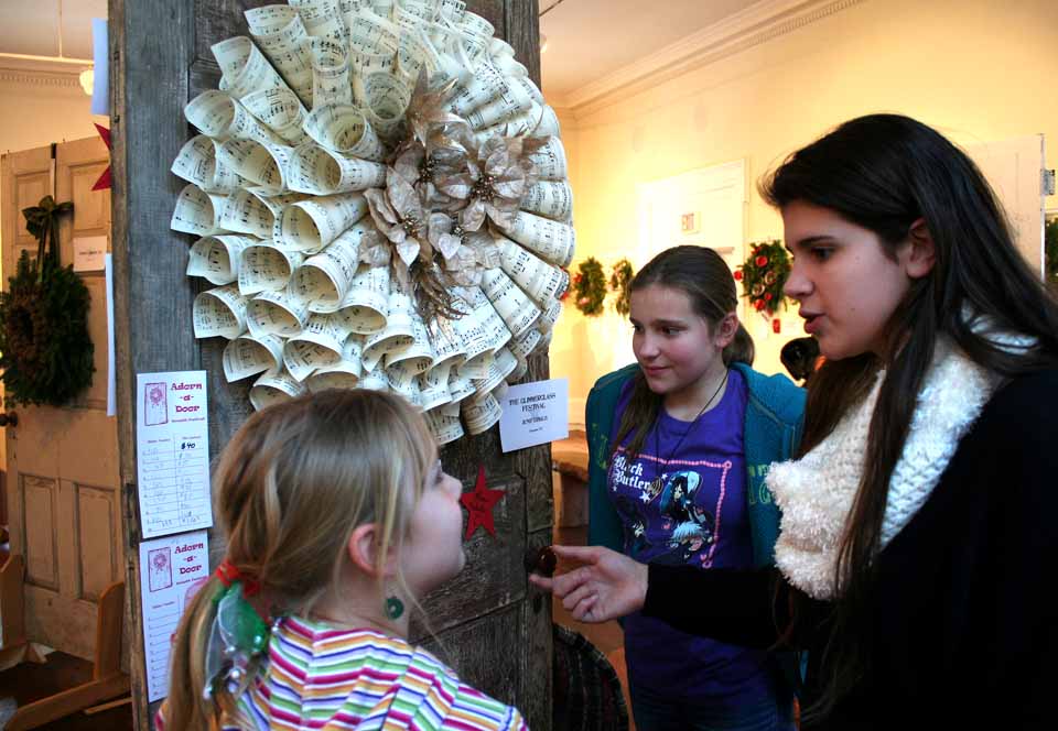 You have until 4:15 today, just a few minutes, to bid on the 138 wreaths in this year's Adorn-A-Door event at the Cooperstown Art Association. This wreath, put together from musical scores by the Glimmerglass Festival's June Dzialo, brought some of the heaviest bidding. Here, Braeden Victory is instructed in the process by the Bischoff sisters. (Jim Kevlin/allotsego.com)