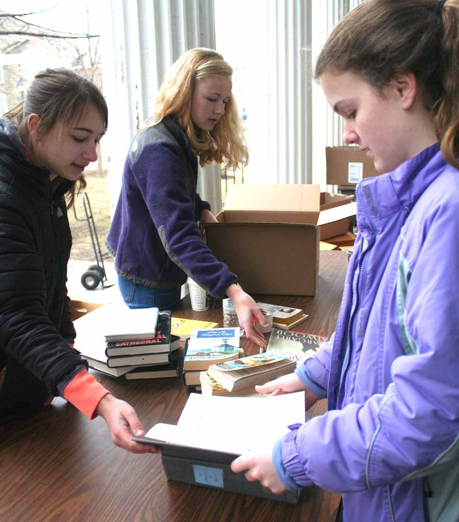 Volunteers – from left, Sophia Lesko, Grace LeCates and Kelly Mooney – sort books this morning on the porch of 22 Main, in preparation for the Friends of the Library's annual Fourth of July Weekend book sale.  Two more book dropoffs are planned before then.  (Jim Kevlin/allotsego.com)