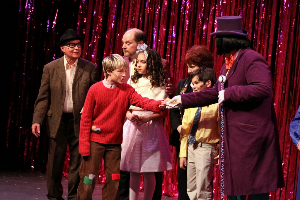 Charlie Bucket (Henrey Wagner) hands his golden ticket to Willy Wonka (Benjamin Burke) at the start of Act 2 of Orpheus Theatre's production of Roald Dahl's Willy Wonka on Sunday afternoon. Grandpa Joe 9Bill Goertemoeller), Mr. Salt (James Iversen), Veruca Salt (Mikayla Web), Ms. Teavee (Anita Levine) and Mike Teavee (Andrew Web), stand by awaiting entry into the chocolate factory. (Ian Austin/allotsego.com)