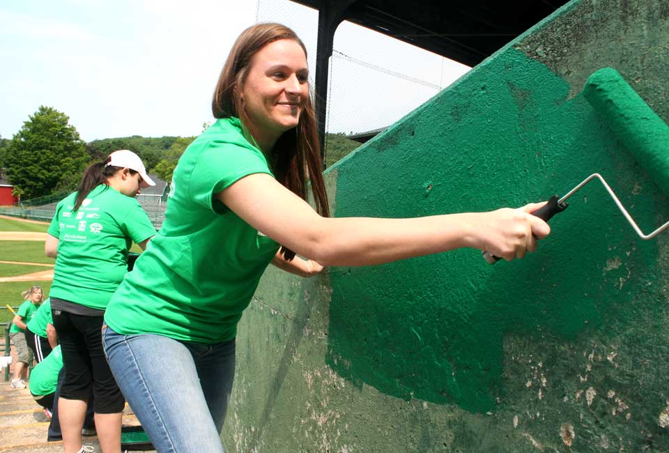 Ashlee Lansing, who handles sports bookings for the Holiday Inn, Albany, helps paint a bleacher wall at Doubleday Field this morning.  She was part of the Tourism Cares contingent.  (Jim Kevlin/allotsego.com)