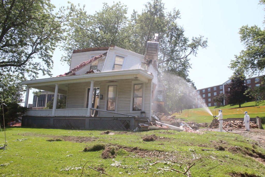 The last pieces of 67 East st. fall under the bucket of the Excavator, operated by Mike French, Unadilla, while David Pierce , Oneonta, hoses the debris to keep dust down under the eye of Michael Sherlock, Oneonta. The demolition of two former student residential houses located at 67-69 East St. by Eastman and Associates was completed Thursday and marks the first step in Hartwick Colleges' plan to redo the entrance area to the college. A nearby retaining wall will also be removed and leveled off, then being turned into a green space. (Ian Austin/ allotsego.com)