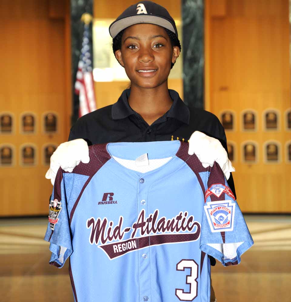 This morning in the Hall of Plaques, Mo'ne Davis holds up the jersey she donated to the Baseball Hall of Fame last year; she was in Cooperstown today with her team, the Anderson Monarchs, as part of their Civil Rights Barnstorming Tour, dramatizing young people, about their age, killed a half-century ago during resistance to desegration in the South.  (Milo Stewart Jr./Baseball Hall of Fame)