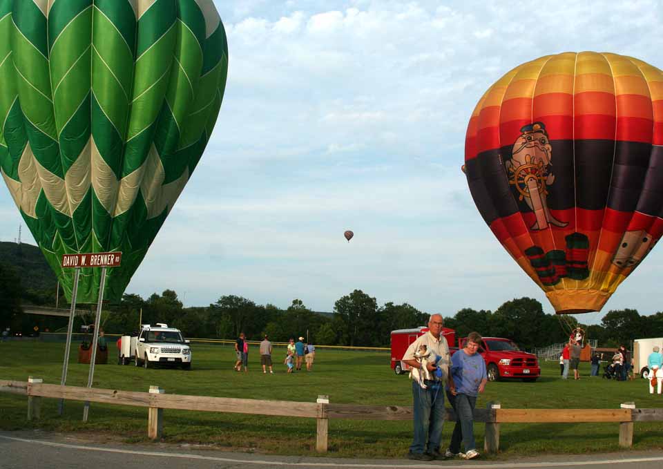 In Oneonta, Walton's  Norman Groat, with Rufus' in his arms, and Norman's wife Doris, cross James Georgeson Avenue in front of Damaschke Field as the hot air balloons are brought to ground for the evening.  Saturday, the Hometown Fourth of July Celebration begins with a parade at noon, ending with fireworks at dusk.  (Jim Kevlin/allotsego.com)