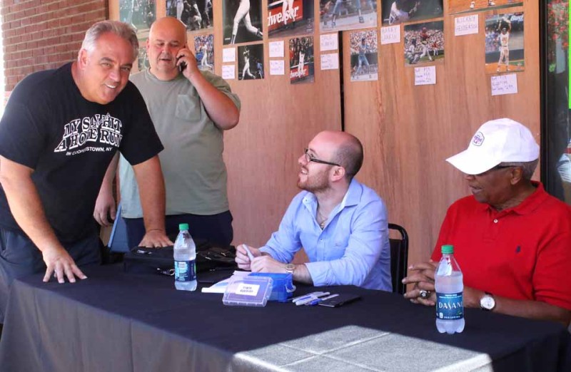 AND SO IT BEGINS! Frank Robinson, former Oriole and Cincinnati Red, was first on the signing scene this morning, set up for autographs in front of the former TJ's Place. At left is the building's new owner, Perry Ferrara. (Jim Kevlin/allotsego.com)