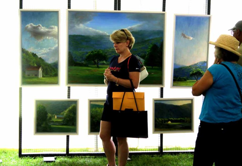 Cooperstown's Joan Dwyer is framed by one of Jessica Dalrymple's landscapes as she contemplates other at Art on the Lawn, underway behind The Fenimore Art Museum until 5 today, followed by a Lake Effect Concert at 7 – The Patti Van Tassel Jazz Quartet on the lakeside Lucy B. Hamllton Amphitheatre. (Jim Kevlin/allotsego.com)