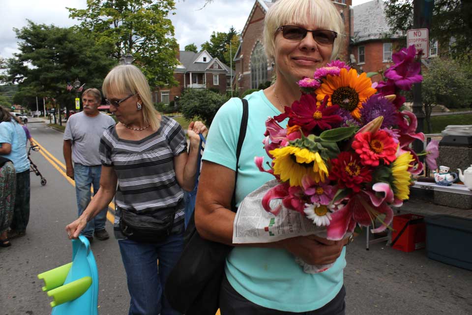 Deb Greene of Otego picked up fresh flowers at this morning's Grand & Glorious Tag Sale on Main Street, Oneonta, where dozens of vendors and hundreds of shoppers sold everything from junque to antiques. Behind her is sister Marty Mahar, Oneonta. (Jm Kevln/AllOTSEGO.com)
