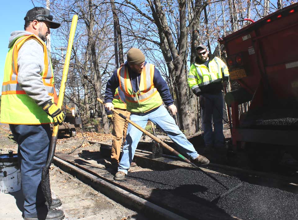 For years, drivers have experienced filling-shaking jolts at the railroad crossing at the west end of Cooperstown's Walnut Street, that ends today. Cooperstown & Charlotte Valley Railroad and village crews are collaborating in bring the crossing up to par. Here, village crew memberjChris Satriano spreads blacktop between ties placed by the railroad crew, at Street Superintendent Mitch Hotaling, right, and Byron Bubencik look on. The job is expected to be done by the end of the day. (Jim Kevlin/AllOTSEGO.copm)