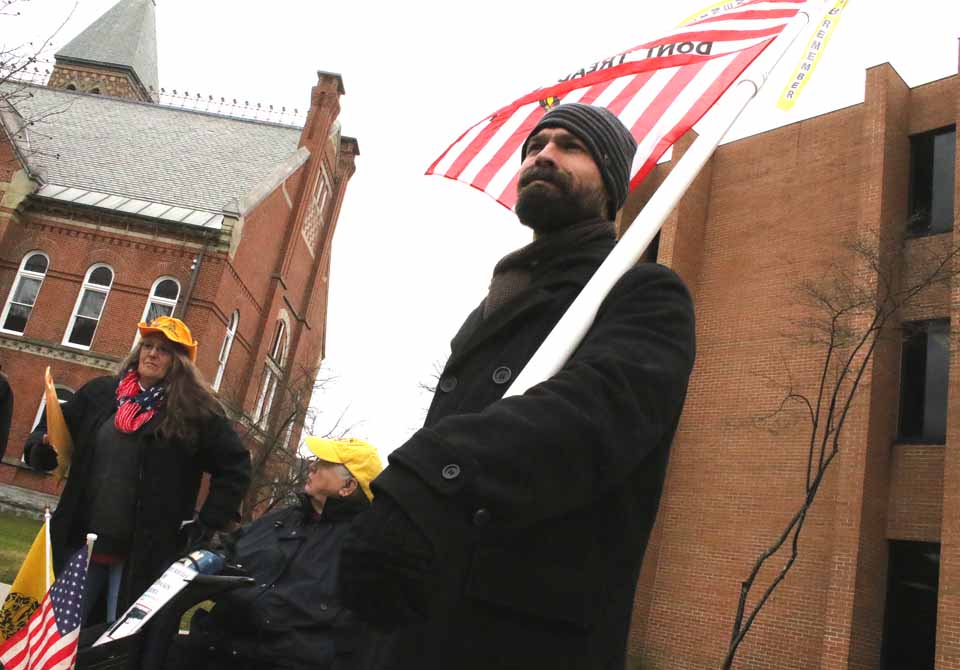Vicent Rasulo of East Patchogue, L.I., bears the "Don't Tread on Me" flag at the tax protest underway at this hour in front of the County Office Building ,n Cooperstown. About 20 people are in attendance, including Marie Ajello, Richfield, and Bob Force, Gilbertsville, who lost their properties in the 2014 tax auction, despite offering to pay back taxes. At left is Judy Pepenella, also of Long Island, a founding board member of the Conservative Society for Action. In the middle is Jeanne Bridger, Town of Maryland (Jim Kevlin/AllOTSEGO.com)