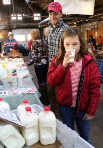 Grace Shipman of Pierstown (dad Mike is behind her) tries out fresh milk at Cooperstown Farmers' Market last Saturday, provided by Mountain View Farm, Richfield Springs. (Jim Kevlin/AllOTSEGO.com)