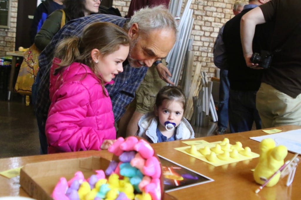 Manny Peligra, Oneonta and Senior Associate Director of Admissions at Hartwick college, looks over the submissions to the 16th annual Peep Show with his granddaughters Bella and Illiana in the Anderson Center this afternoon. The show, judged by Elizabeth Ayer, featured a wide range of artworks created in honor of or with the marshmallow treats. (Ian Austin/AllOTSEGO.com)