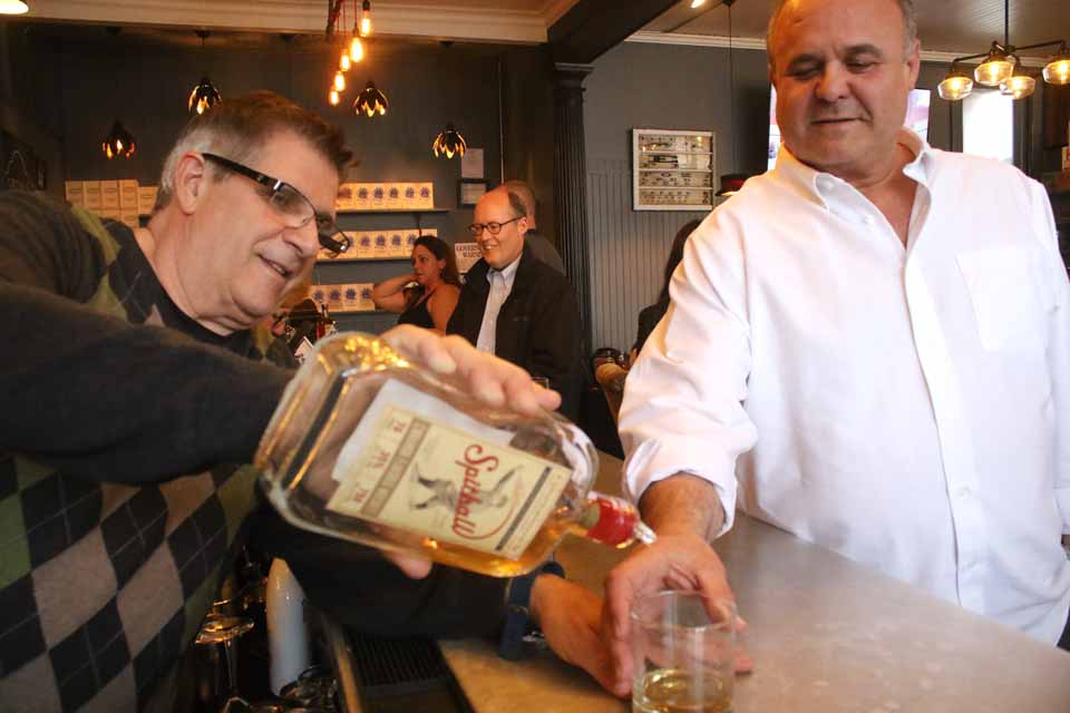 Cooperstown Distillery proprietor Gene Marra pours samples of "Spitball," the distillery's new blended whiskey, this evening at the Cooperstown Beverage Exchange at Main and Pioneer. Rich Abbate, Cooperstown, prepares to take a sip. "Spitball," developed to take advantage of a growing demand for flavored whiskeys, was introduced in New York City earlier this month. (JIm Kevlin/AllOTSEGO.com)