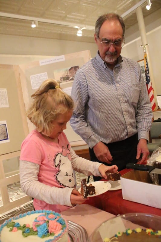 Claire Smith cuts herself a slice of cake under the supervision of Bob Brzozowski at the well attended GOHS Cake Walk during Fabulous First Friday yesterday evening. Claire had herself quite a night, winning two cakes for her and her family. (Ian Austin/AllOTSEGO.com)