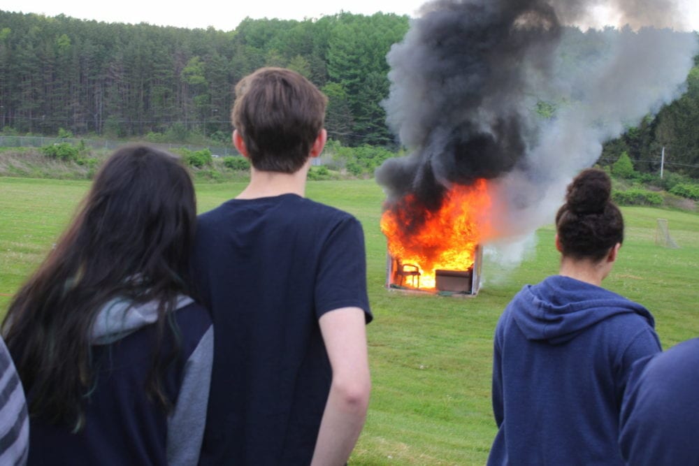 Members of the OHS senior class Michelle Chen and Dan Mazzei, left, watch as a mock dorm room goes up in flames during a live burn at the high school this morning. The burn illustrated how quickly a fire can spread through a living space. In this case the room was completely consumed in less that three minutes. The live burn was the second part of a Life and Safety class taught by Cpt. Brad Smith of the Oneonta fire department, to teach seniors kitchen, fire and dorm safety. Highlights included proper cooking of food, how to use fire extinguishers, heeding alarms and more. (Ian Austin/AllOTSEGO.com) 