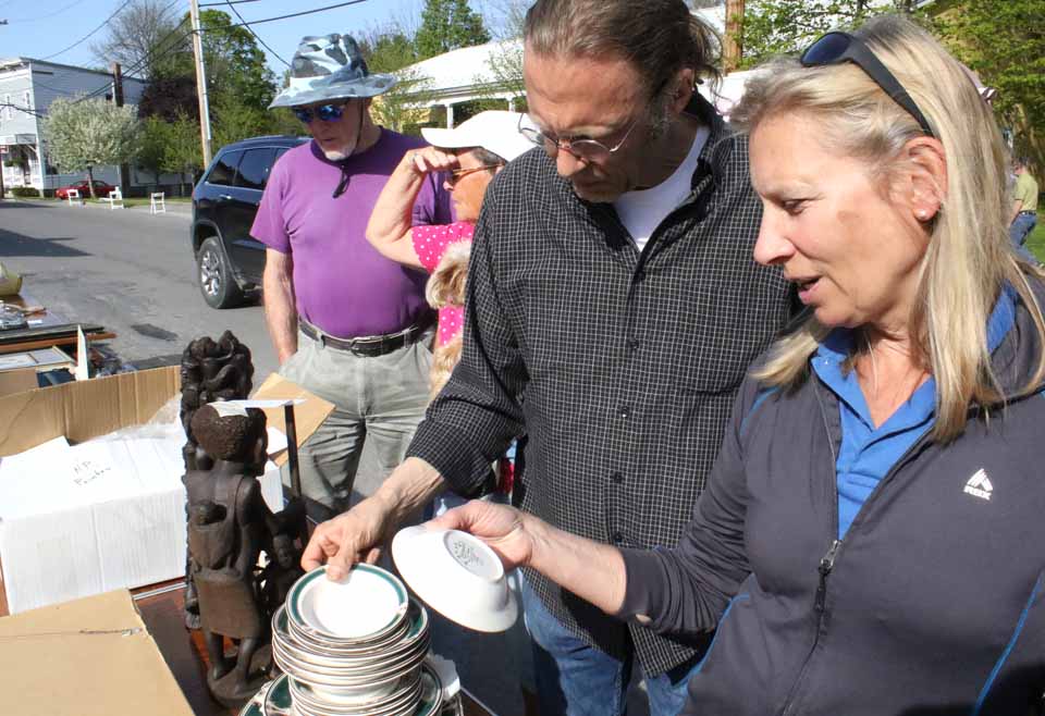 Would-be bidders review the offerings at the Cooperstown Rotary Club's "Spring Fling" Auction, due to begin at 5:30 p.m. today at One Railroad Ave.  In the foreground, Rotarians Tom Lieber and Ellen Tillapaugh examine a set of dishes.  Behind them are Lynn DeLong, visiting from Mayfield, with Gail Olin, Fly Creek, and her dog Teddy.   Tickle Me Pink barbecue and Red Shed brewery are offering refreshments.  The main event, the "Spring Fling" festival, begins at noon Saturday.  Railroad Avenue will be closed off for the occasion.  (Jim Kevlin/AllOTSEGO.com)