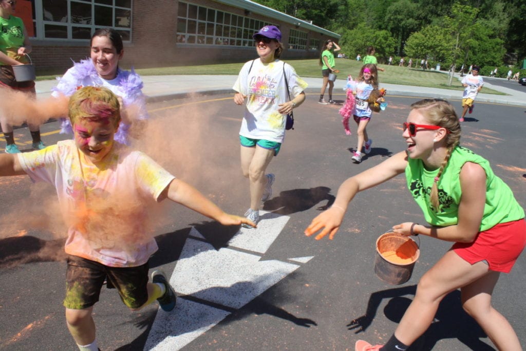 Liz Millea throws pigment at the runners as they pass by her station in the Cooperstown Color Run this morning. (Ian Austin/AllOTSEGO.com)