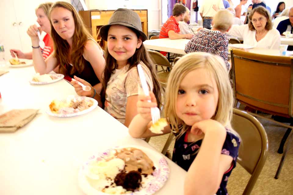 The Moyer girls, from right ,Alice, 5, Madeleine, 12, and mom Emily partake of ice cream and cake at the Cooperstown Presbyterian Church Ice Cream Social, which continues until 8 p.m. at Church and Pioneer, the traditional opener to the Fourth of July Weekend. In this afternoon's downpour, organizers had moved all the tables into the chapel; but, with an hour of sunshine, many of the tables were moved back onto the front lawn. (Jim Kevlin/AllOTSEGO.com)