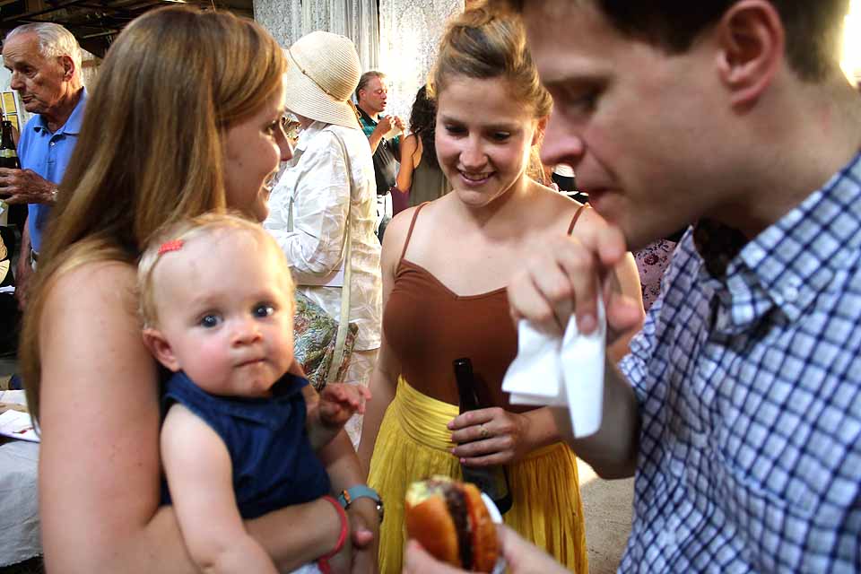 Dad Eric Bland, a Bassett medical student, partakes of the offerings at the fourth annual Local Foods, Local Spirits this evening, a benefit for the Cooperstown Farmers' Market --and he feeds an occasional tidbit to daughter, Alice, 11 1/2 months. Alice is being tended by Laura Bland and Abby Bland, two of Eric's sisters. (Jim Kevlin/AllOTSEGO.com)