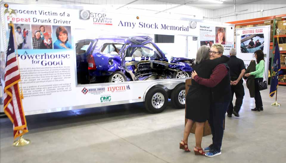 Kim Robinson of Prolifiq Signs, which did the graphics on the Amy Stock Memorial trailer, hugs Amy's sister Eileen Anania, who led the effort to turn a tragedy into teaching moments, as Tuesday dedication ceremony was about to begin. (Jim Kevlin/AllOTSEGO.com)