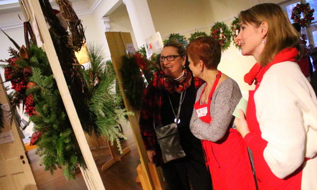 A cheerful Margaret Savoie, left, got in the holiday spirit with her daughter, Jackie, as they bid on wreathes at Adorn-A-Door Wreath Festival this afternoon at the Cooperstown Art Association. With them, center, is volunteer Tara Santello. The annual event, which invites visitors to bid on handmade wreathes from local artists & businesses, raises money for art scholarships. (Ian Austin/AllOTSEGO.com)