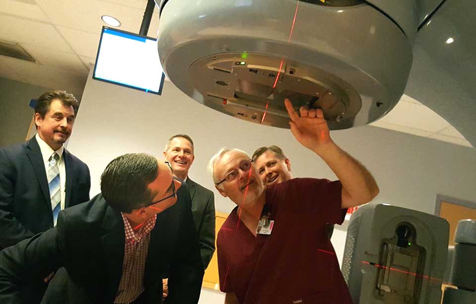 Mark Tryniski, left, Community Bank president/CEO, and Radiation Therapist Roy Doremus, right, look into the eye of the Foxcare Cancer Treatment Center's linear accelerator.  Tryniski was at FoxCare today to deliver the final $20,000 payment of a $100,000 pledge the bank made toward the 2012 purchase of the advanced apparatus, which more accurately pinpoints tumors and treats them, avoiding the need for more intense radiation.  Behind them are, from left, Jeff Lord, Commercial Banking team leader, Joe Sutaris, bank vice president, and Jeff Joyner, Fox Hospital president.   "These cutting-edge treatments are changing the landscape of cancer treatment, making radiation therapy an open for many more patients than ever before," said Joyner.   He also thanked the Dewar and Robinson Broadhurst foundation for helping cover the accelerator's price.  (Ian Austin/AllOTSEGO.com)
